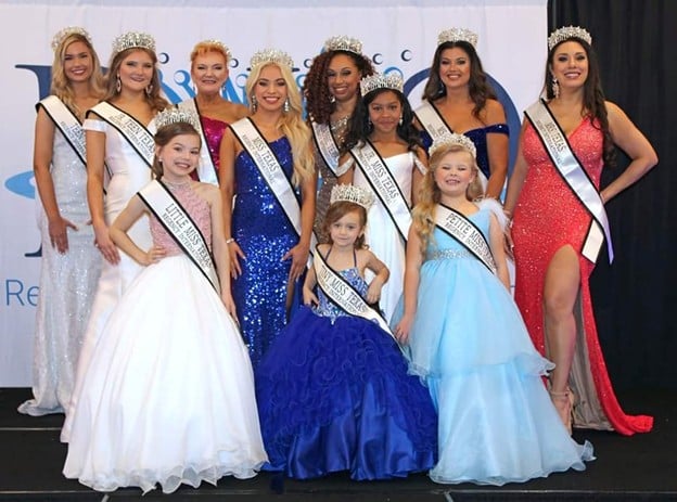 Group of pageant contestants in formal dresses and crowns.